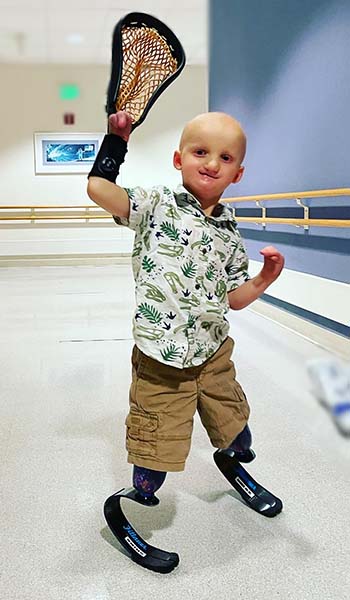 Child with prosthetics in a hospital hallway with a lacrosse net on his hand.